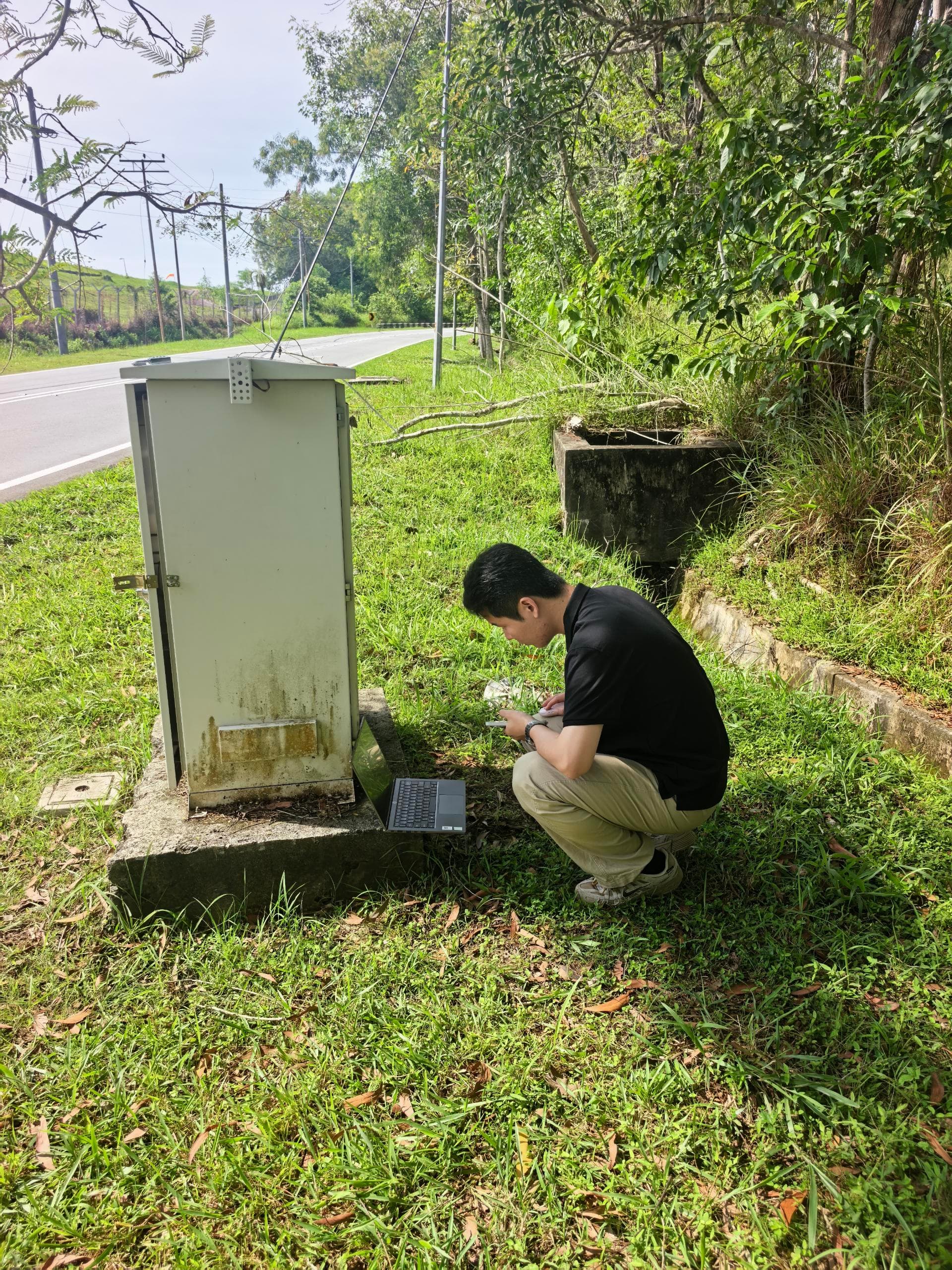 Engineer checking an outdoor control cabinet with a laptop